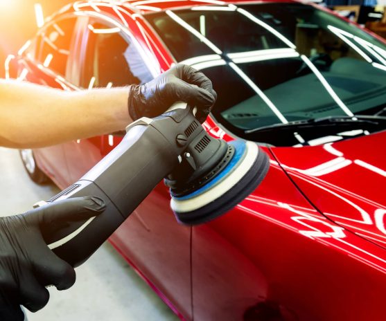 Car service worker polishes a car with orbital polisher.